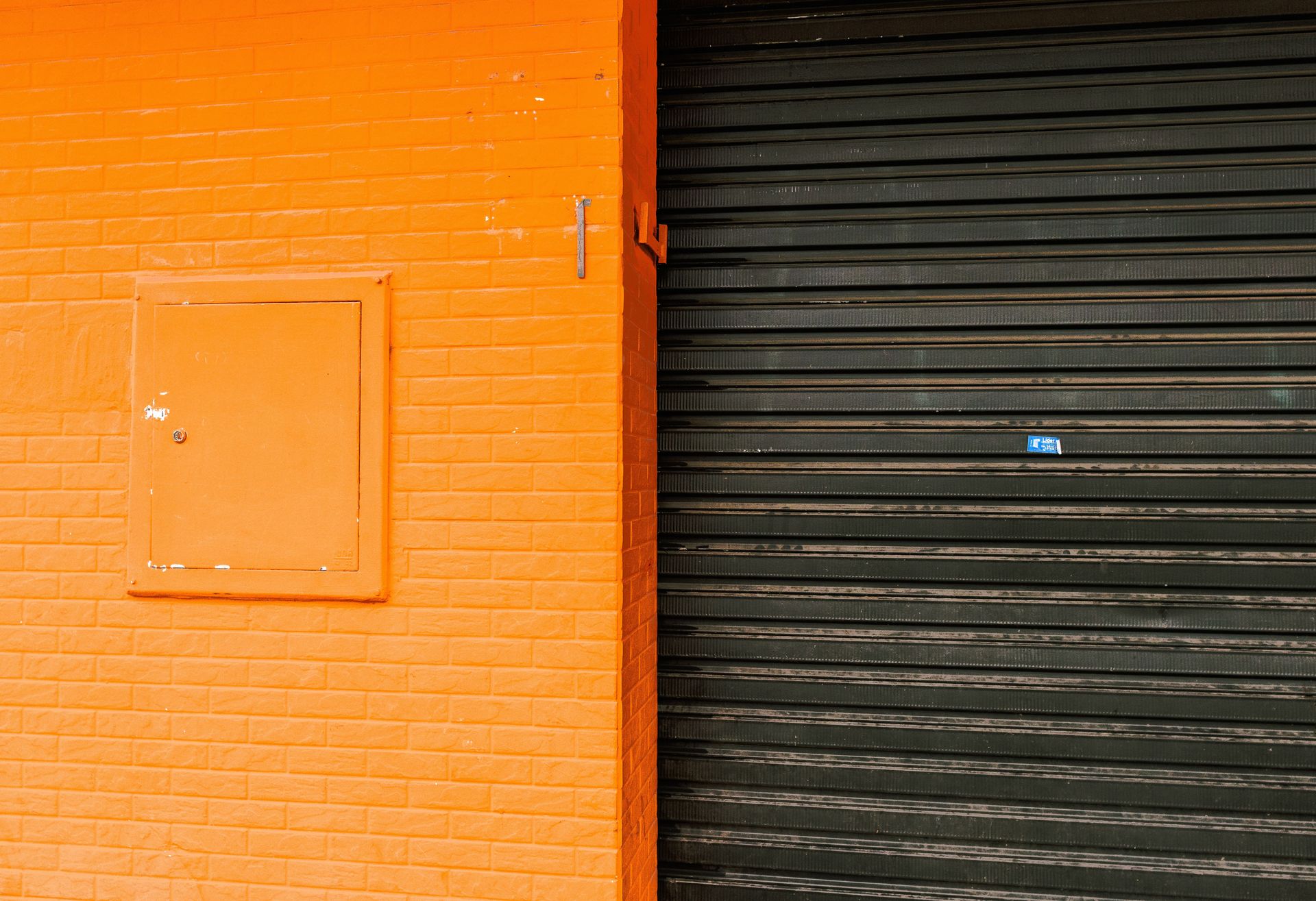 An orange-painted wall with imitation brick texture and a contrasting black roller door in an urban setting.